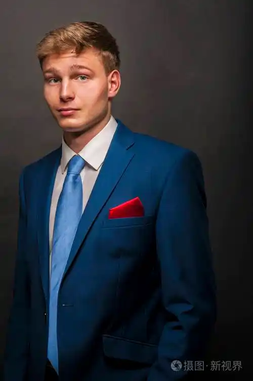 年轻的帅哥穿着蓝色西装在深色背景下微笑