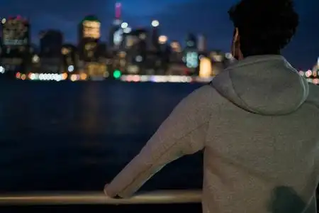 在晚间城市背景下, 身着灰色运动夹克的年轻人的背影在城市环境中以