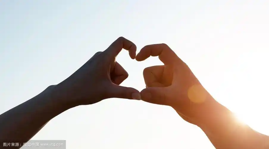 双手合在一起,在夕阳的天空前,创造一颗心