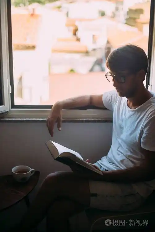 戴眼镜的年轻帅哥在窗户附近看书. 周末概念