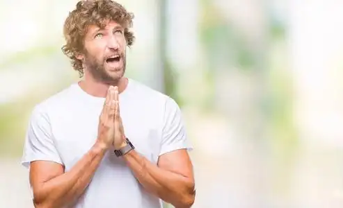 模特男人在孤立的背景下乞讨和祈祷,双手一起祈祷,脸上充满希望的表情