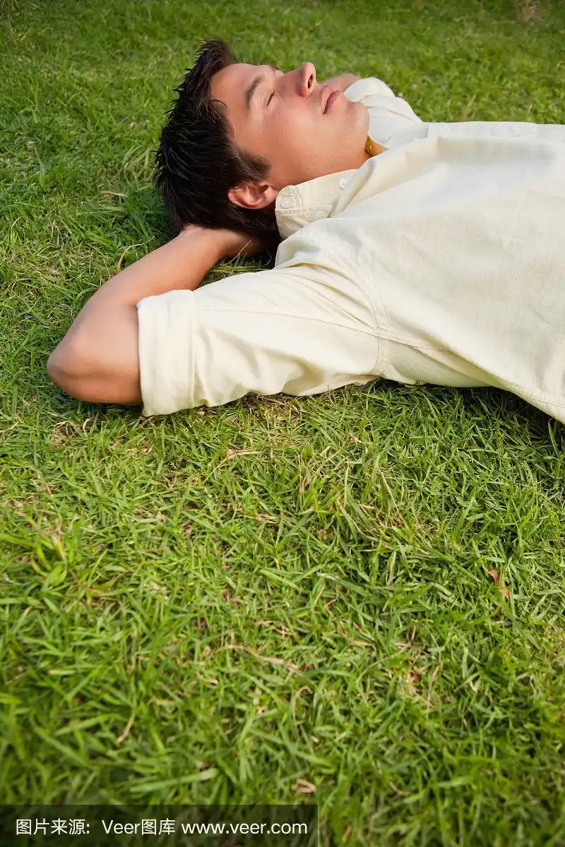 一个人躺在草地上,闭着眼睛,双手放在脑后