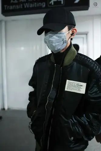 千玺身穿墨绿色夹克,内搭黑色高领,戴黑色棒球帽配灰色口罩,耳朵里塞