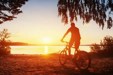 男孩骑上自行车在日落时两个漂亮的女孩,在沙滩上自行车,在篮子里的